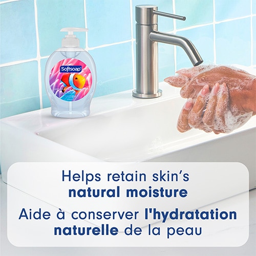 Softsoap Aquarium bottle sitting on a white sink next to a faucet, with hands lathering under running water. Text: "Helps retain skin’s natural moisture".