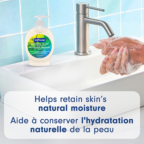 Softsoap aloe bottle sitting on a white bathroom sink next to a faucet, with hands lathering under the tap. Text: "Helps retain skin’s natural moisture".