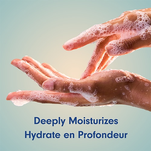 Close-up of two hands washing with rich, foamy white soap lather against a gradient background, with the text "Deeply Moisturizes".