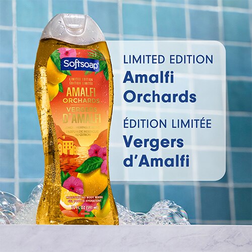 Une bouteille de nettoyant corporel hydratant Softsoap « Amalfi Orchards » (Édition Limitée), placée sur un fond de carreaux bleus parsemé de bulles de savon. Le texte indique « Limited Edition Amalfi Orchards » et « Édition Limitée Vergers d’Amalfi ».
