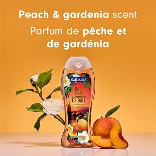 Le flacon de gel douche Bali Bliss est placé entre une pêche fraîche et des fleurs de gardénia blanc. Un texte en anglais et en français indique : Parfum de pêche et de gardénia.