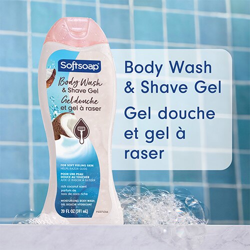 Flacon de Gel douche et gel à raser Softsoap « Rich Coconut », posé contre des carreaux de salle de bain bleus, avec des bulles. Texte en anglais et en français : Body Wash & Shave Gel, Gel douche et gel à raser.