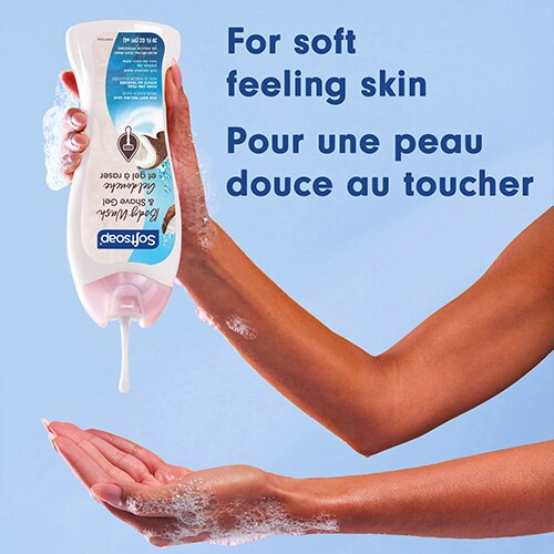 Une personne verse du savon liquide Softsoap blanc et hydratant de la bouteille dans sa main. Texte en anglais et en français : Pour une peau douce au toucher.
