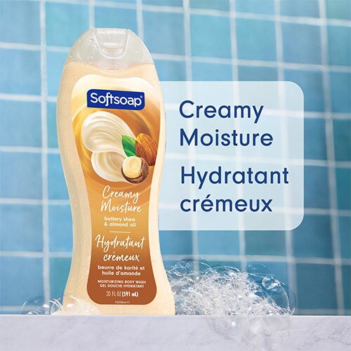 Flacon Softsoap au karité onctueux et à l'huile d'amande, dans une douche aux carreaux bleus, entouré de bulles. Le texte, en anglais et en français, indique : Creamy Moisture, Hydratant crémeux.