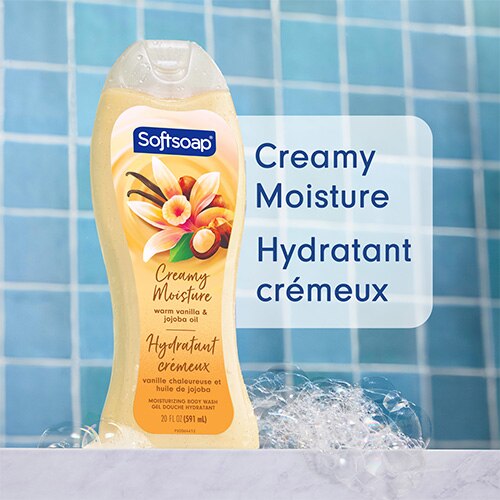 Une bouteille de 20 onces du nettoyant corporel hydratant Softsoap « Warm Vanilla and Jojoba Oil », sur un fond de carreaux bleus parsemé de bulles. Un grand texte sur la droite indique « Creamy Moisture », accompagné de sa traduction française : « Hydratant crémeux ».