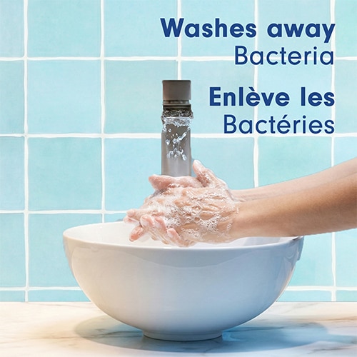 Deux mains lavées sous l'eau courante dans une vasque blanche devant un mur de tuiles bleues. Texte : « Washes away Bacteria / Enlève les Bactéries ».