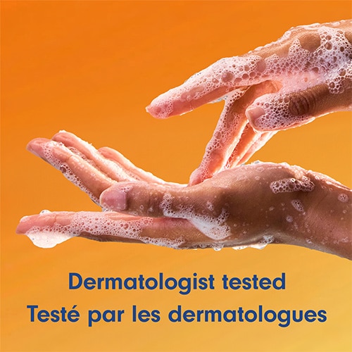 Deux mains se lavant avec une mousse blanche riche sur fond orange uni. Texte : « Dermatologist tested / Testé par les dermatologues ».