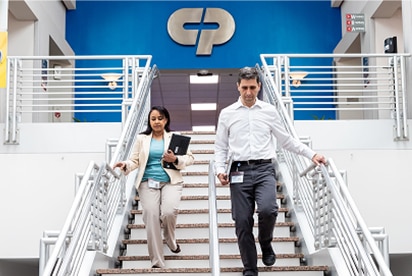 Deux professionnels d'entreprise descendent des escaliers dans un bureau moderne avec le logo Colgate-Palmolive en arrière-plan.